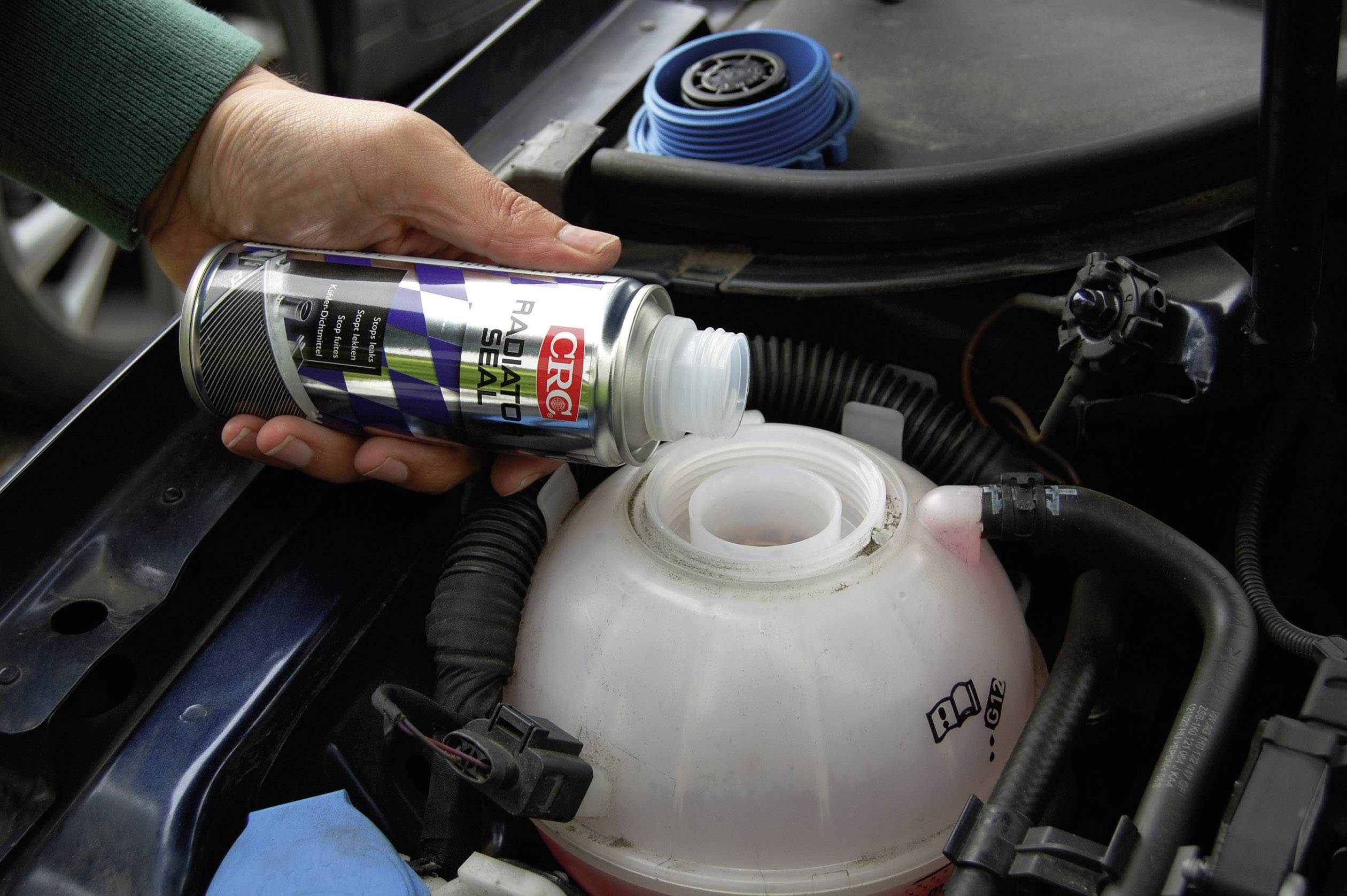 Une personne verse du liquide de refroidissement dans le réservoir d'expansion d'une voiture. Le réservoir est déjà partiellement rempli.