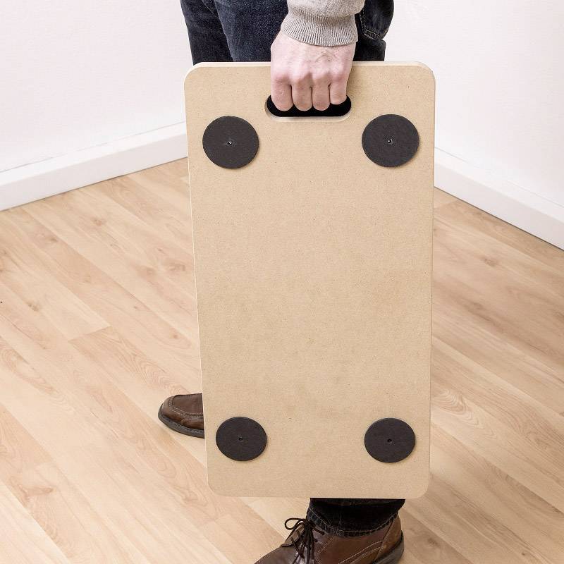 Une personne tient une petite table rectangulaire avec des pieds noirs et la déplace sur un plancher en bois.