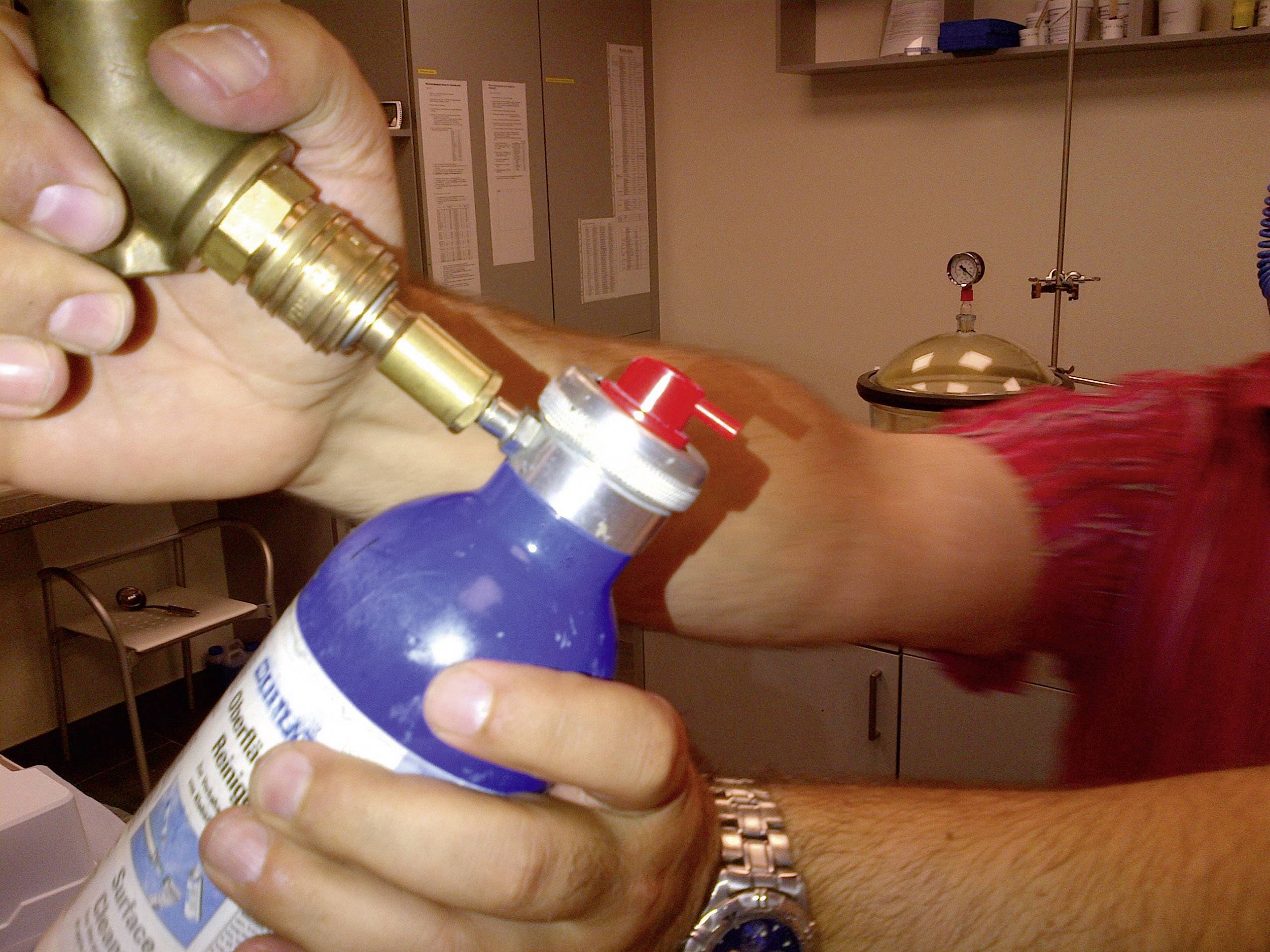 Une personne illustre le processus de recharge d'une bouteille d'extincteur avec un raccord de valve dans un espace de travail.