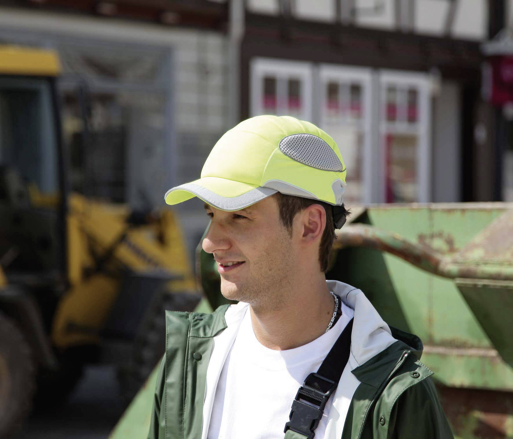 Un homme portant un casque de sécurité jaune se tient sur un chantier de construction. À l'arrière-plan, on distingue une pelleteuse et des bâtiments.