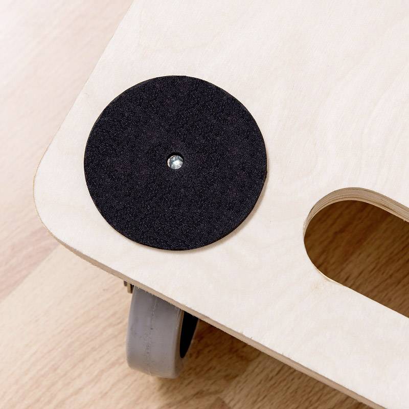 Une plateforme en bois montée sur roulettes et dotée de supports en feutre noir rond sur un sol stratifié. Une découpe circulaire sert de poignée.