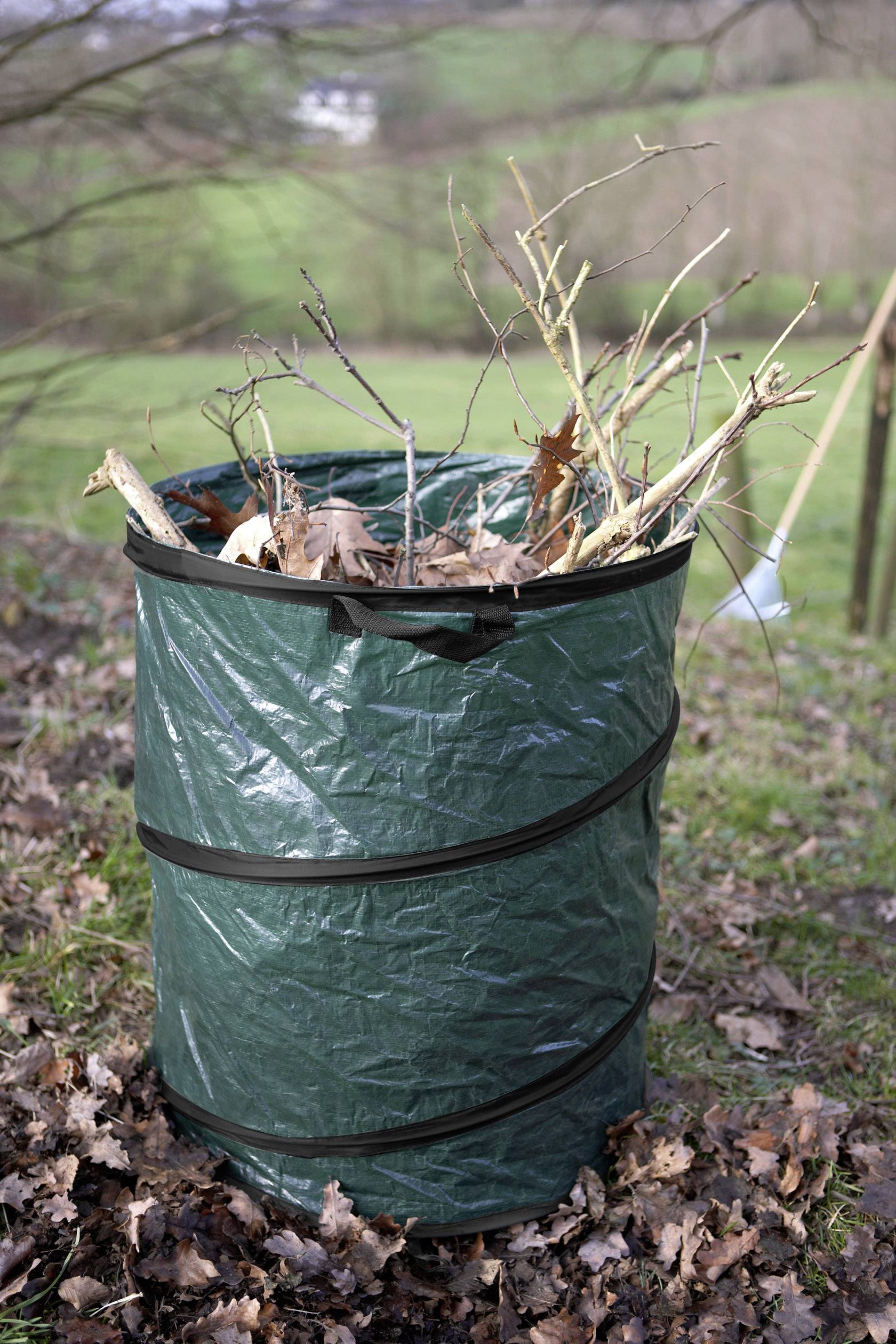 Un sac de jardin vert rempli de branches et de feuilles est posé sur un sol herbeux à l'extérieur.