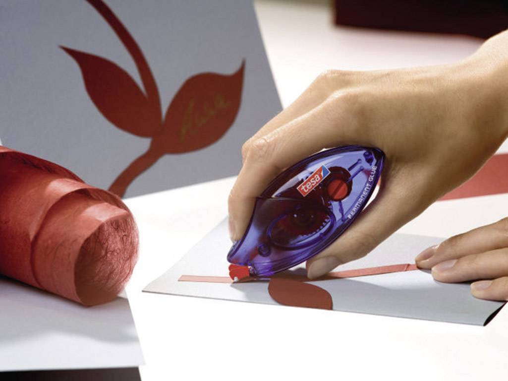 Une main utilise un correcteur à ruban pour marquer une ligne rouge sur du papier gris. En arrière-plan, un motif de feuille rouge est visible.