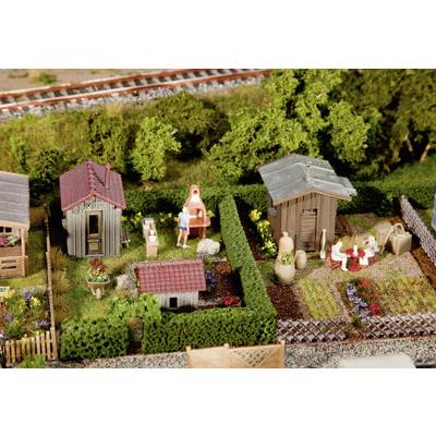 Modèle miniature d'un paysage de jardin avec deux petits bâtiments, des personnes faisant un barbecue et mangeant, entourées de plantes et de clôtures.