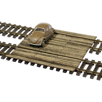 Une petite voiture miniature beige se trouve sur un passage à niveau en bois de train miniature. La voiture a un aspect nostalgique et classique.