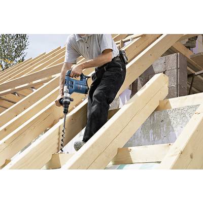 Une personne utilise une perceuse électrique pour faire des trous dans une charpente en bois. Chantier extérieur.