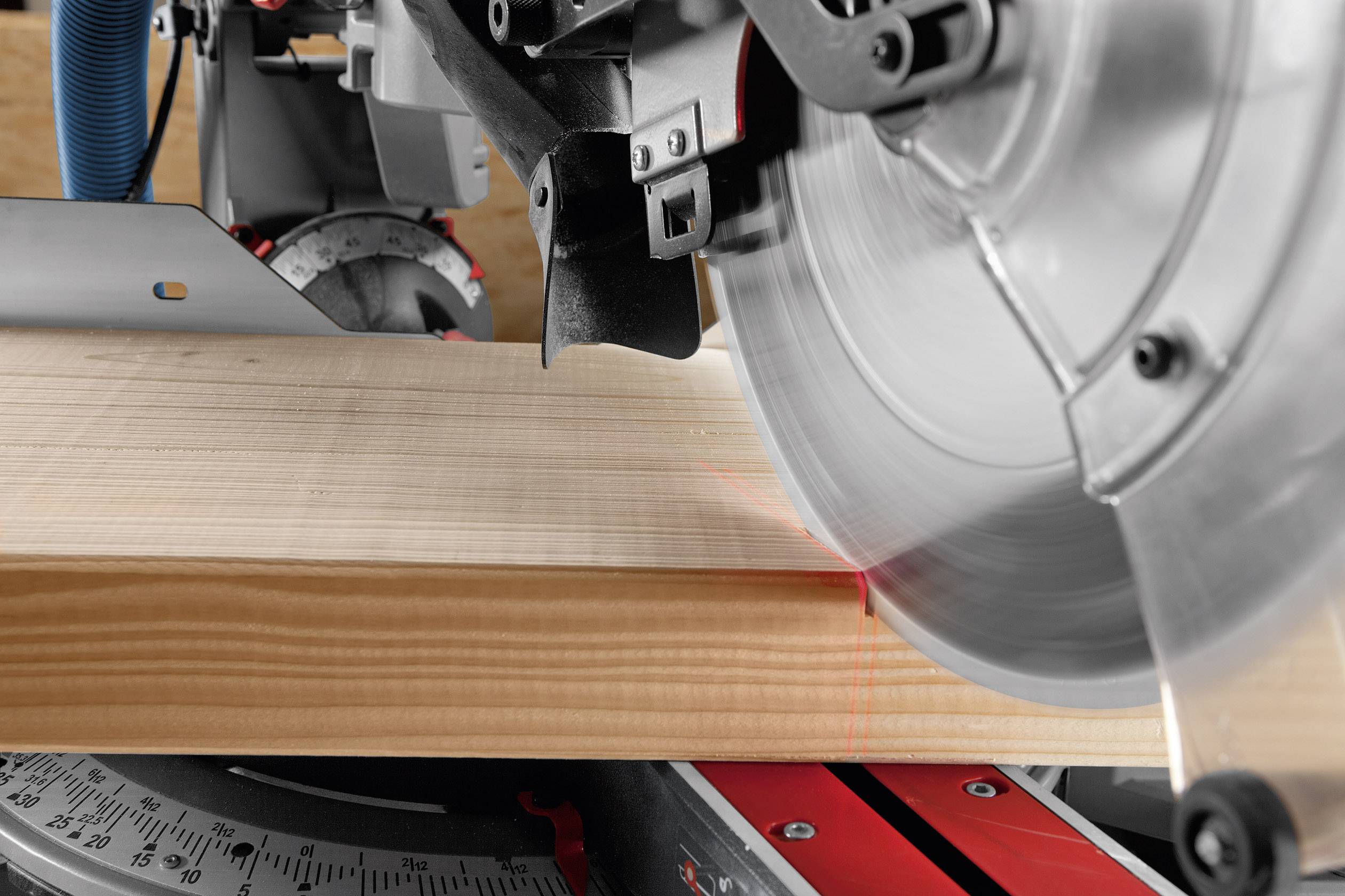 Une lame de scie circulaire électrique coupe précisément une planche de bois. Une ligne laser rouge indique le tracé exact de la coupe.