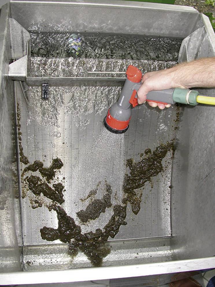 'Une personne projette de la saleté d'une surface métallique à l'aide d'un tuyau d'arrosage, l'eau s'écoulant dans un drain du bassin.'