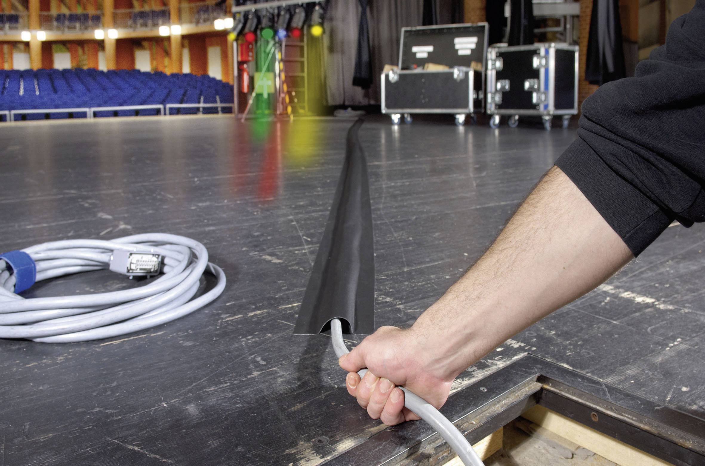 Un câble est installé sur une scène sous une protection. À l'arrière-plan, on aperçoit des sièges vides et de l'équipement technique.