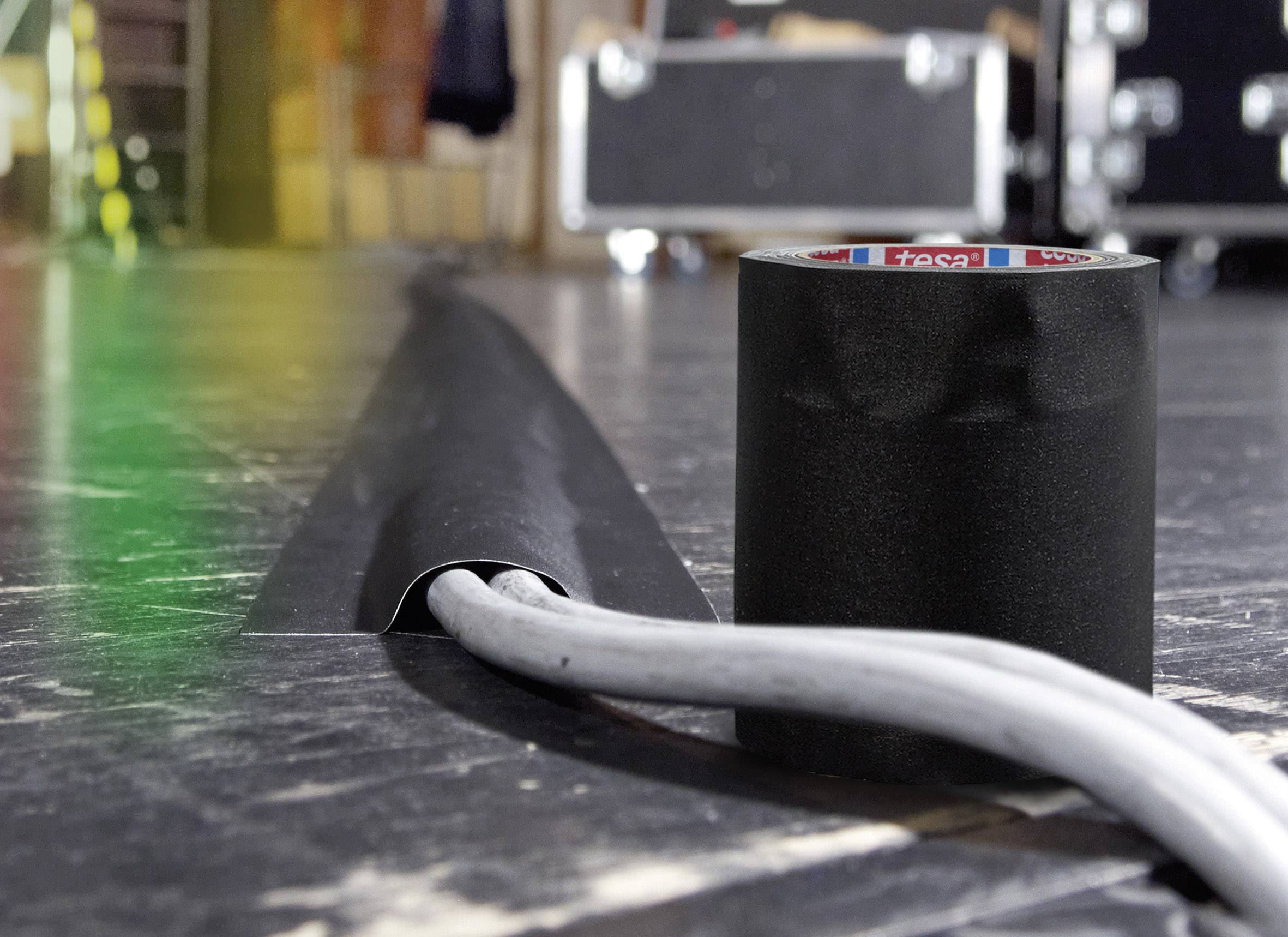 Ruban adhésif noir à côté d'un câble qui traverse un plancher de scène avec un cache-câbles noir. Arrière-plan flou.