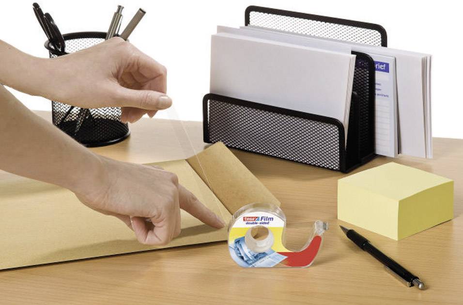 Une personne ferme une enveloppe avec du ruban adhésif sur un bureau où sont posés des stylos, un bloc-notes et un porte-lettres.