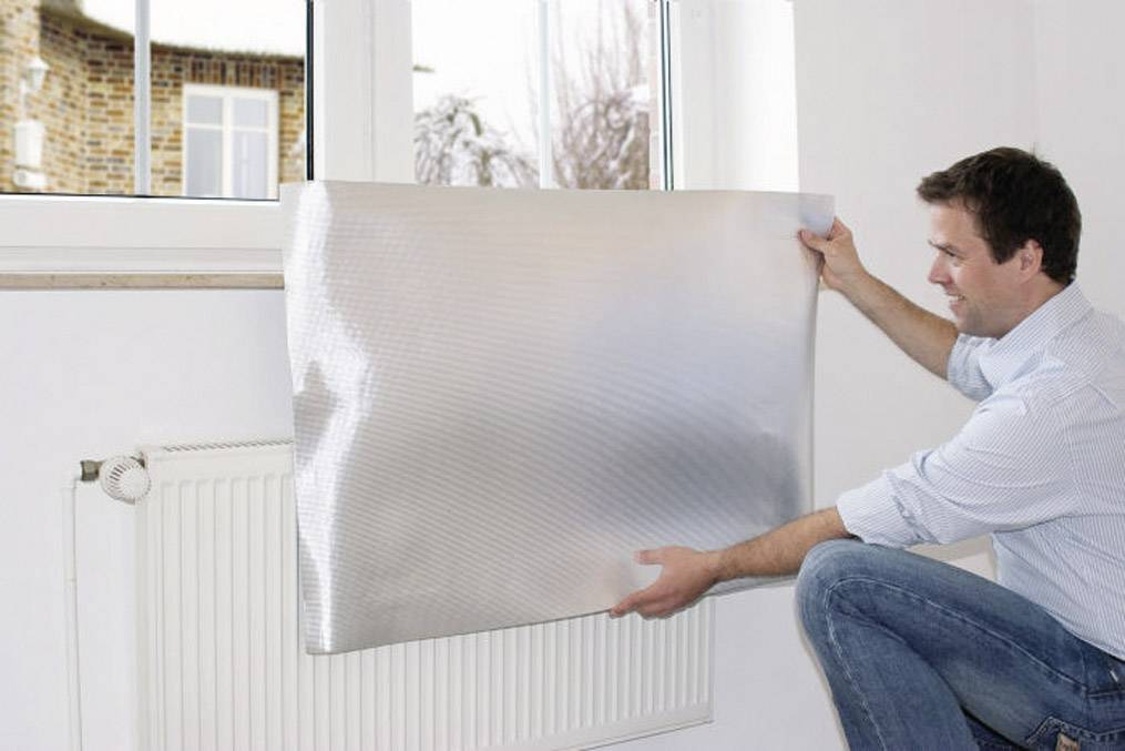 Une personne fixe un film réfléchissant derrière un radiateur afin d'améliorer l'isolation thermique.