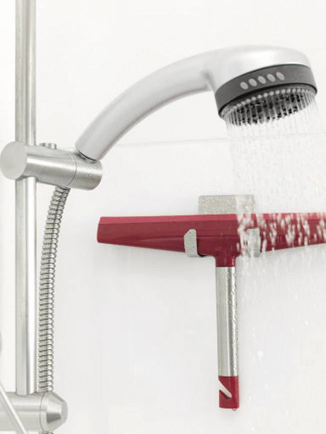 Un pommeau de douche projetant un jet d'eau frappe un raclette fixé sur un support dans une cabine de douche.