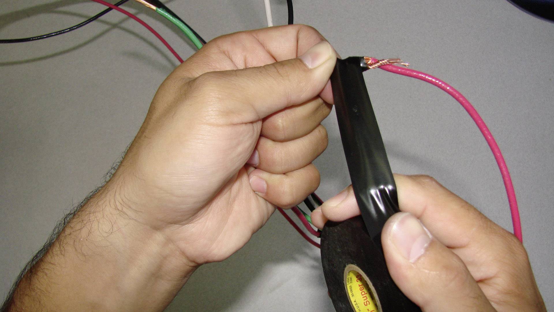 Des mains enroulent du ruban isolant noir autour d'un câble dénudé pour le réparer ou l'isoler.