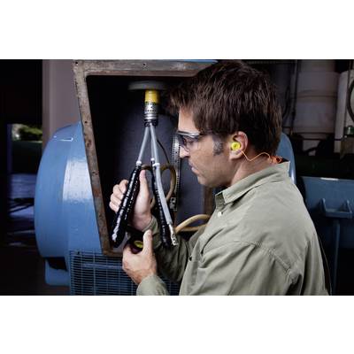 Un homme portant des lunettes de protection et des bouchons d'oreilles vérifie les connexions de câbles sur une grande machine industrielle à l'intérieur.
