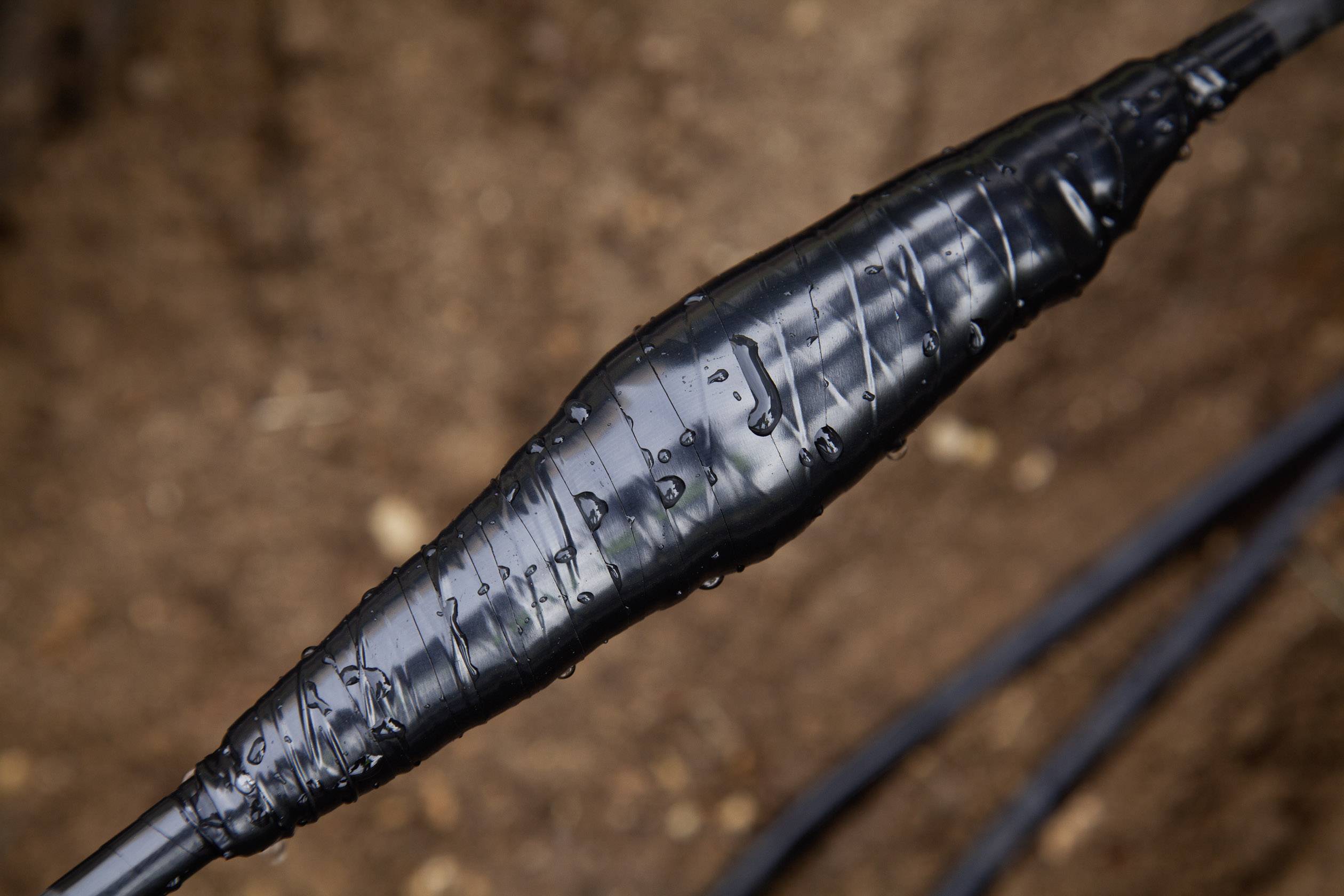 Gros plan sur un câble électrique enroulé d'un isolant noir, installé à l'extérieur dans un environnement humide.