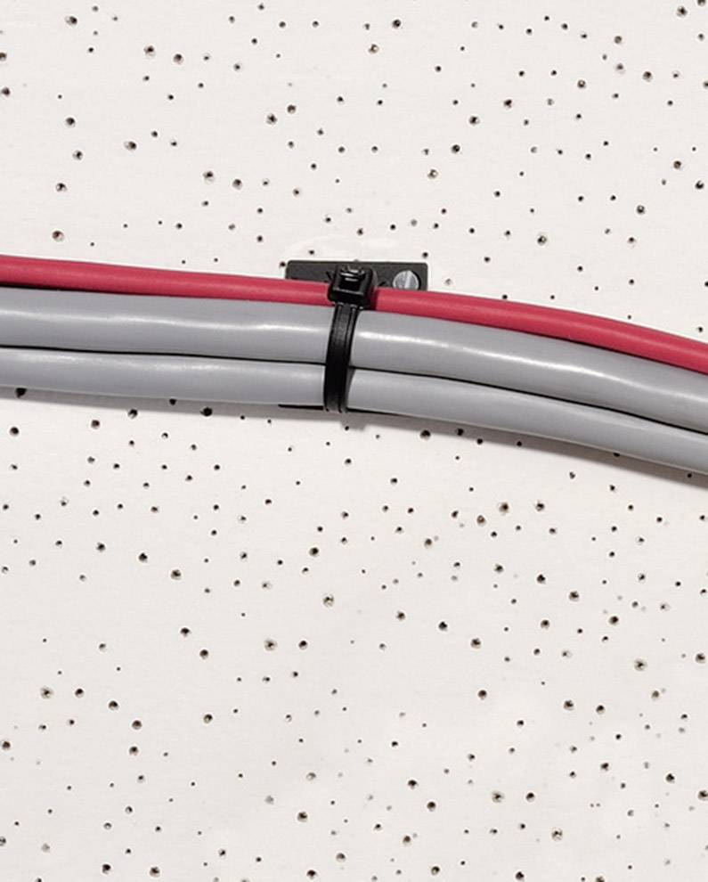 Un cordon gris et un cordon rouge sont fixés avec un serre-câble sur un mur blanc perforé de petits trous.