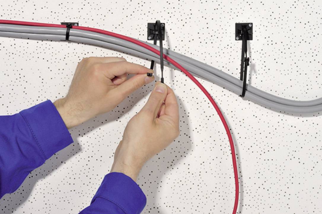 Deux mains fixent des câbles avec des attaches de câble au plafond. Un câble gris et un câble rouge sont visibles.