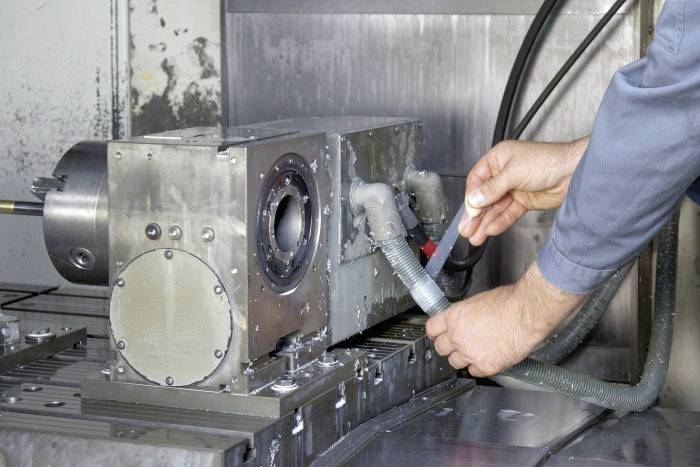 Une personne en tenue de travail installe ou vérifie des tuyaux sur une machine industrielle dans un environnement d'atelier.