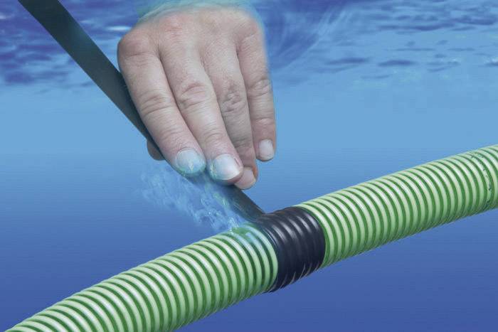 Une main utilise un ruban adhésif noir pour sceller un tuyau rayé vert et blanc sous l'eau.