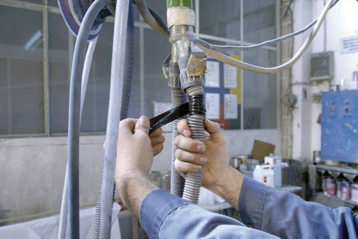 Une personne répare un tuyau dans un atelier avec du ruban adhésif noir pour sécuriser une connexion. Des outils sont visibles en arrière-plan.