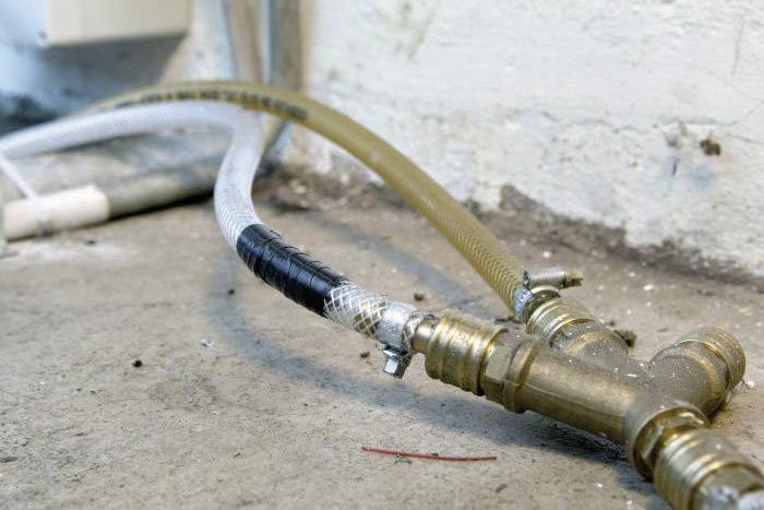 Un tuyau d'eau sanitaire avec deux vannes relie des conduites sur un mur au sol en béton.