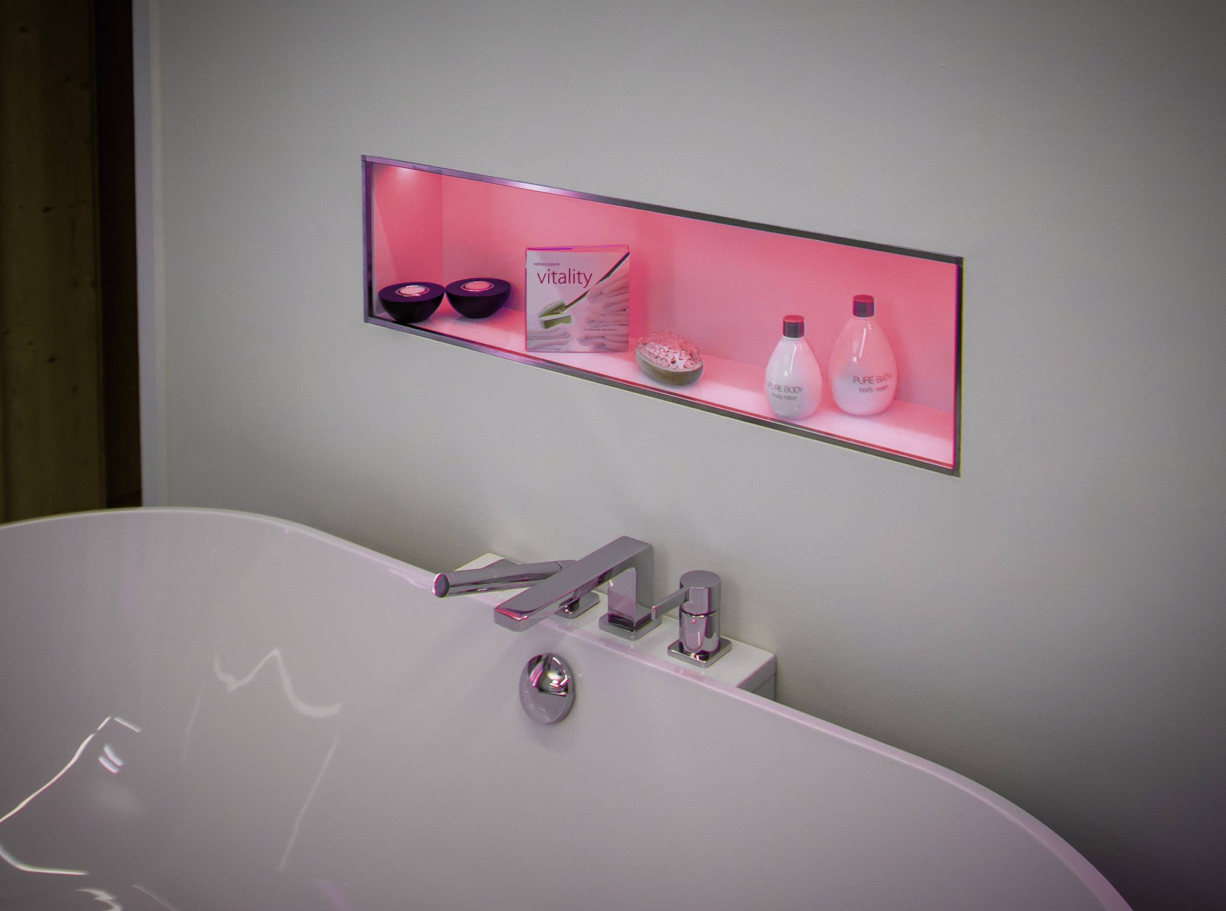 Une baignoire blanche avec un robinet moderne. À l'arrière-plan, une étagère avec un éclairage rouge, contenant des produits de soin et des bols.