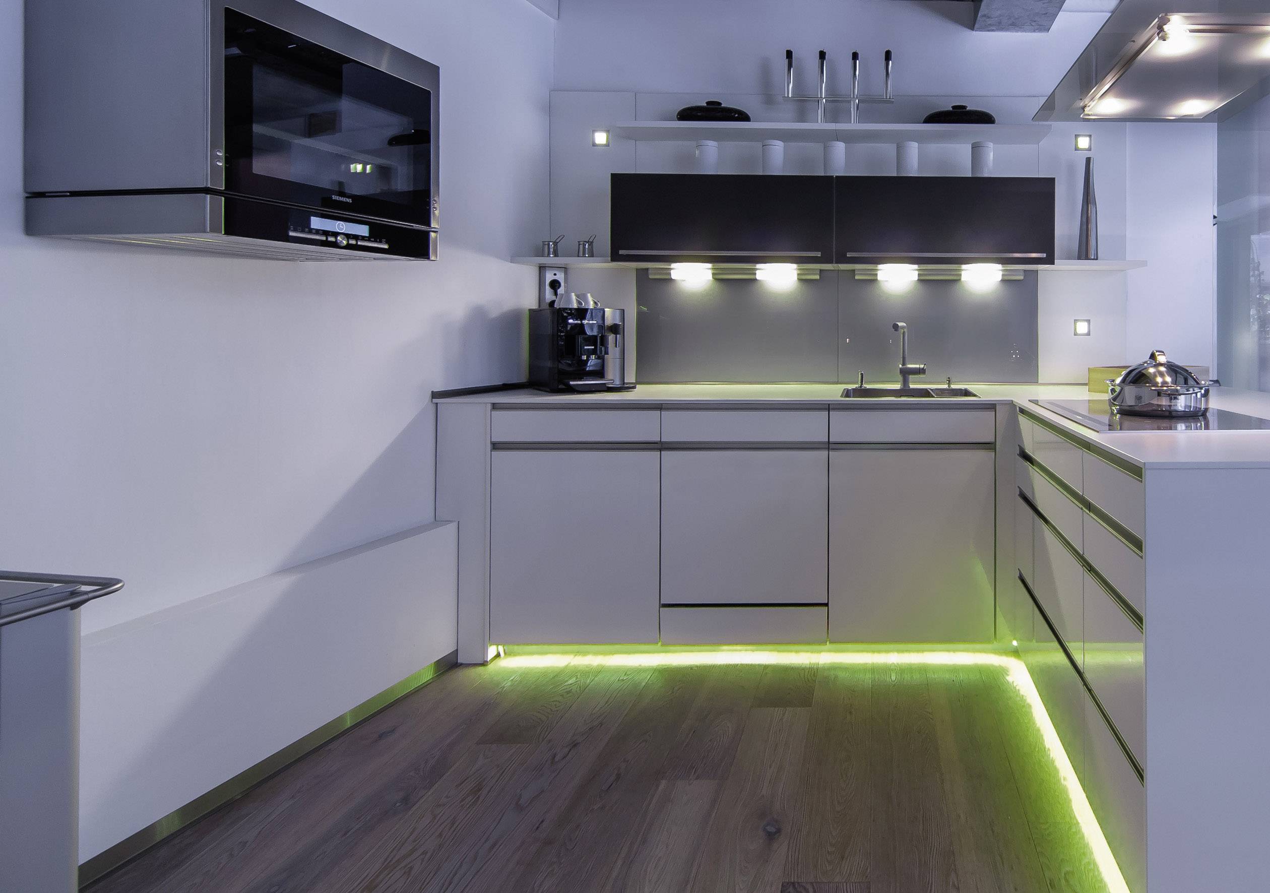 Cuisine moderne aux tons neutres avec des placards et des appareils intégrés. Un éclairage LED vert au sol crée une atmosphère élégante.