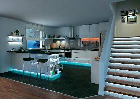 Cuisine moderne avec un îlot central éclairé, des tabourets et un escalier au premier plan. Les murs sont clairs, le sol est carrelé dans des tons foncés.