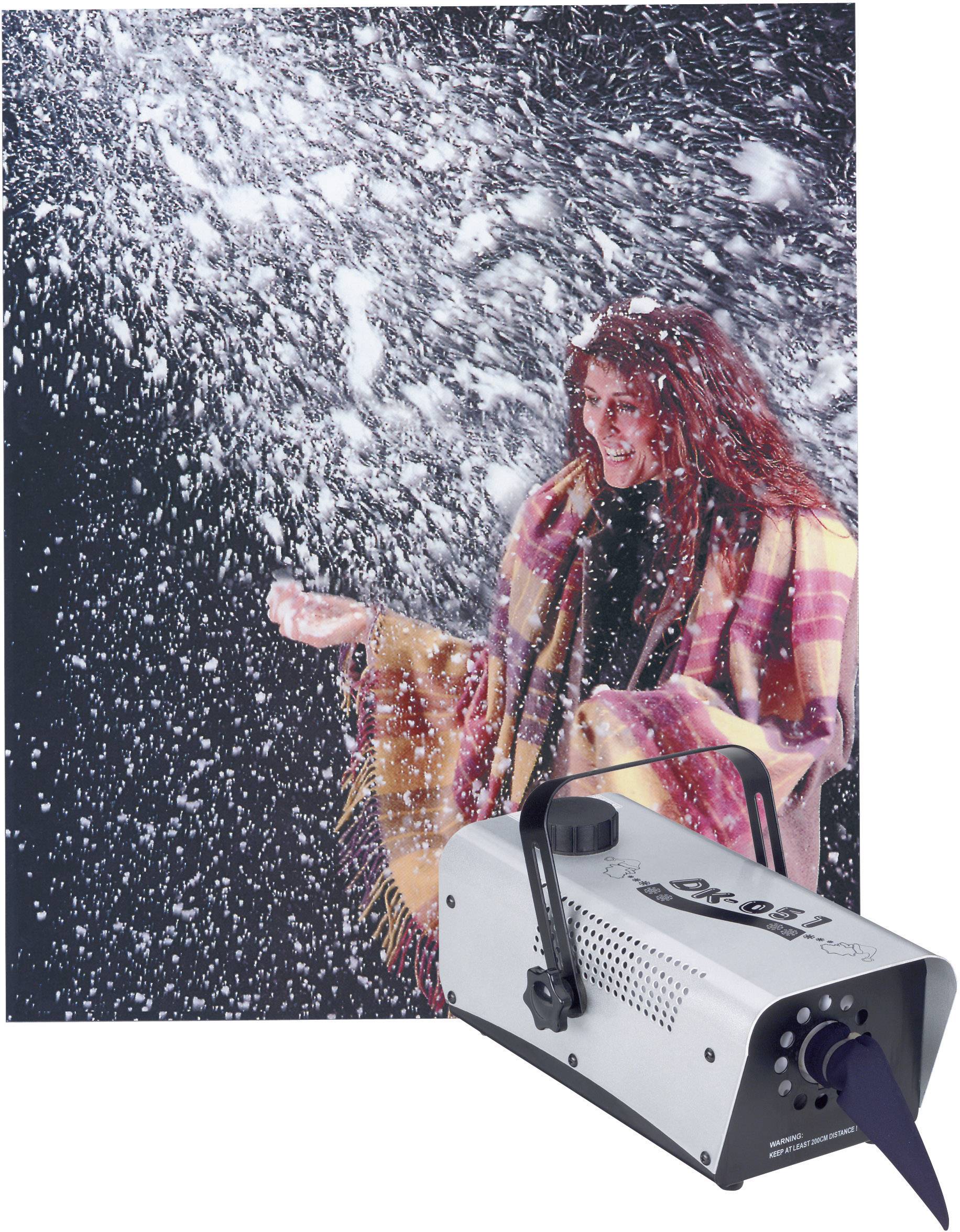 Une femme aux cheveux rouges et portant une écharpe à carreaux se tient dans de la neige artificielle, avec une machine à neige visible devant elle.