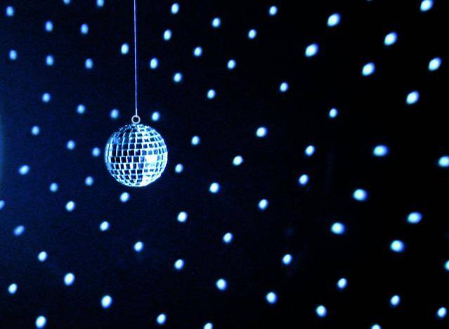 Une boule disco est suspendue et reflète de la lumière bleue dans une pièce sombre, créant un motif de points lumineux sur les murs.
