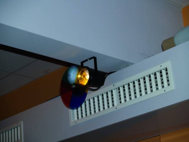 Un projecteur au plafond projette de la lumière à travers une lentille multicolore. Une grille de ventilation est montée à côté.