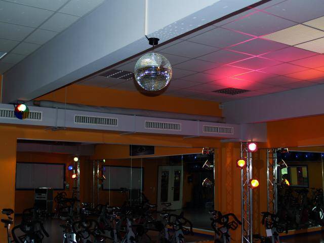 Salle de spinning avec boule à facettes, éclairage coloré et plusieurs vélos de spinning. Aménagement atmosphérique dédié à la musique et au mouvement.