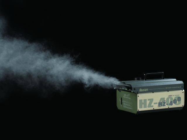 Une machine à fumée émet une fumée dense, visible sur un fond sombre. La fumée se répand vers la gauche.