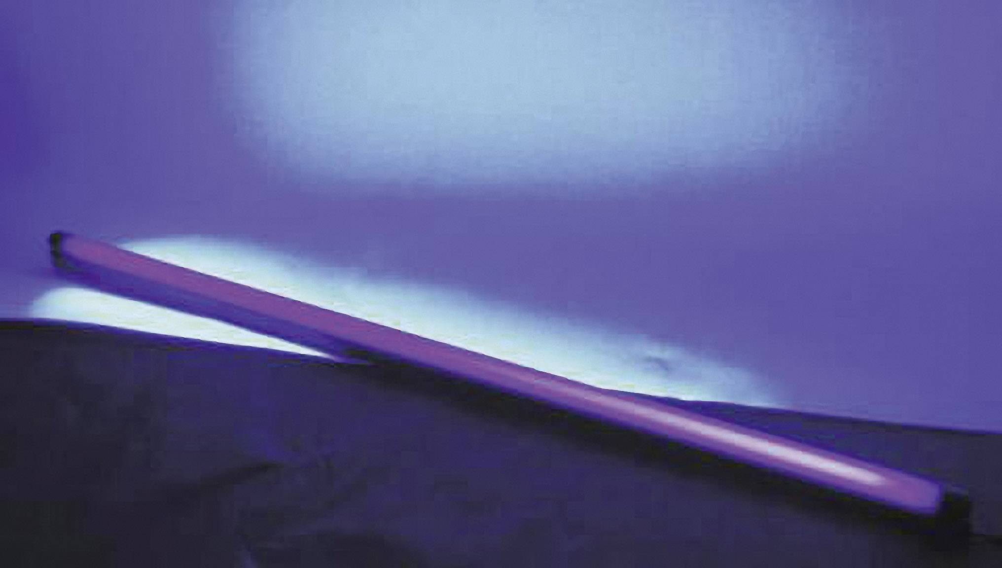 Tube fluorescent luisant bleu-violet dans un environnement sombre, appuyé contre une surface sombre.