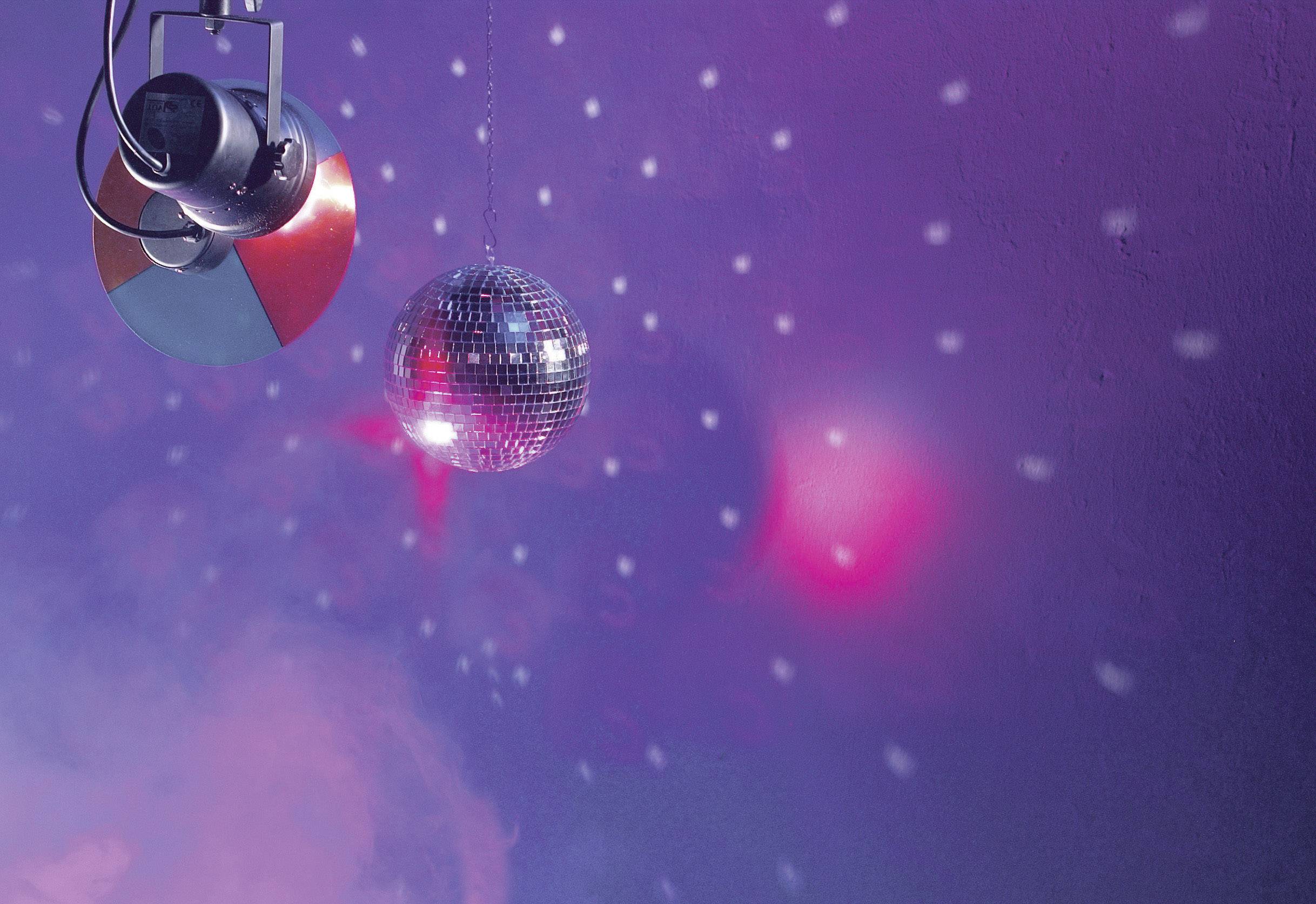 Boule à facettes reflétant des lumières rouges et bleues dans une pièce brumeuse, créant une ambiance festive vibrante avec des effets lumineux scintillants.
