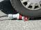 Un pneu de voiture repose sur un connecteur sur une route asphaltée. Le connecteur est rouge et gris et est coincé par le pneu.