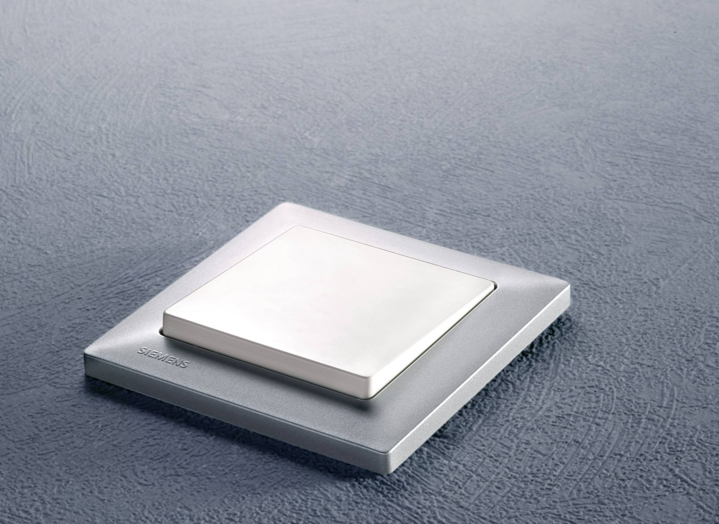 Un interrupteur élégant, carré et métallique à surface plane, monté sur un mur gris texturé.