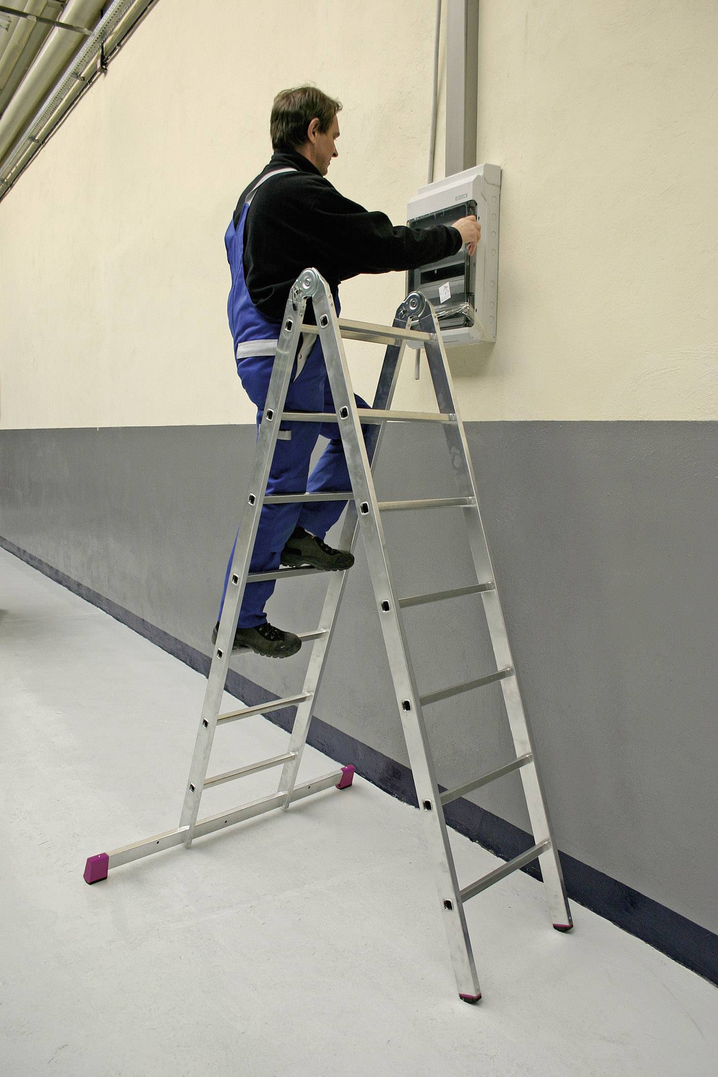 Une personne est debout sur une échelle et travaille sur un boîtier de distribution mural.