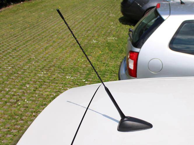 Antenne automatique sur un véhicule blanc garé sur un parking pavé. Une voiture argentée est garée à côté.