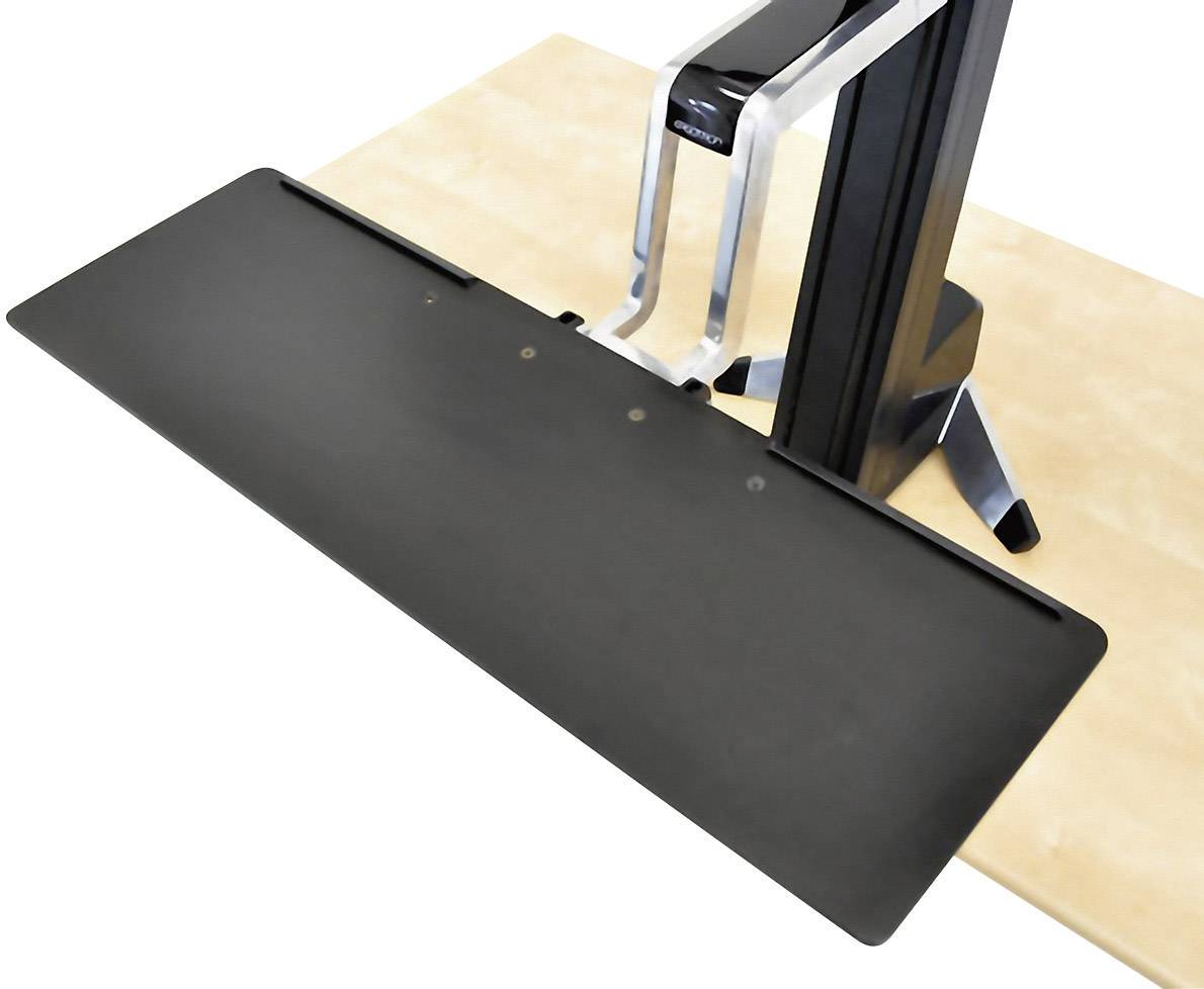 Un accessoire de plateforme noir et rectangulaire, monté sur un support argenté posé sur une table claire ; probablement un équipement de bureau ou de studio.