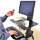 Une personne est assise à un poste de travail informatique, tenant une télécommande à la main. Le bureau est réglable en hauteur.