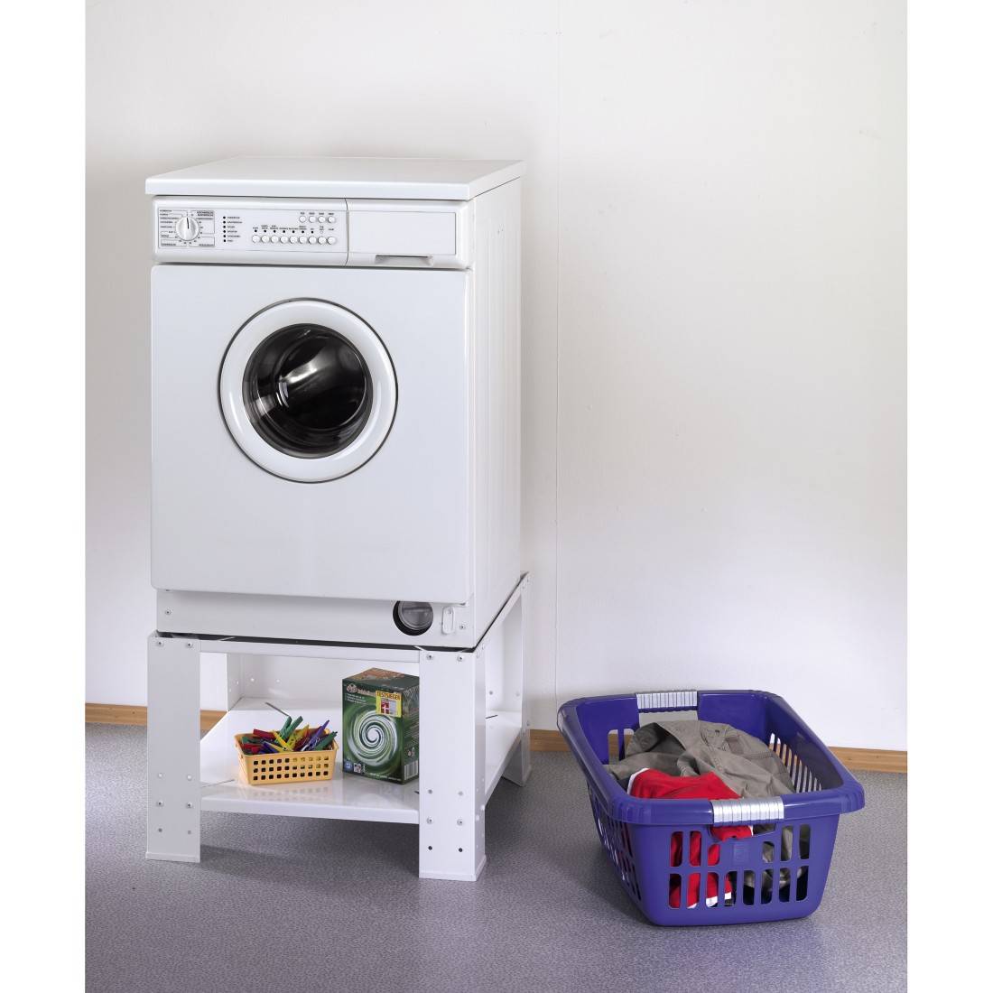 Machine à laver installée sur un socle à côté d'un panier à linge bleu contenant des produits de nettoyage.