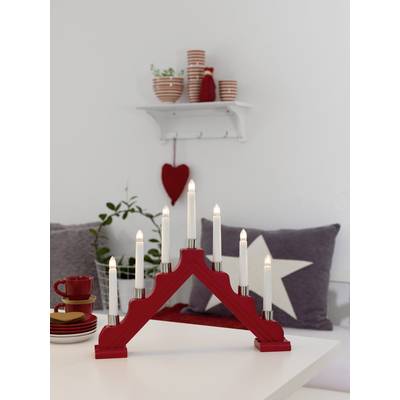 Un arc de bougie rouge à sept lumières est posé sur une table blanche. En arrière-plan, on aperçoit une étagère avec des tasses et des objets de décoration.