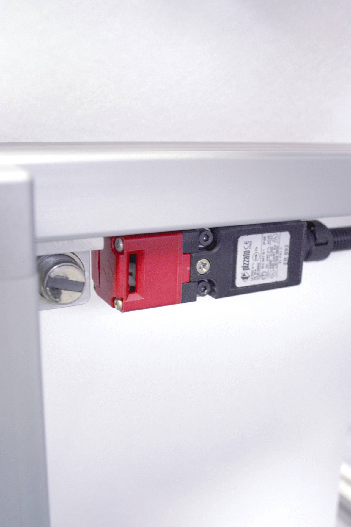 Un interrupteur de sécurité rouge et noir est monté sur un cadre métallique argenté. Un avertissement est visible sur l'interrupteur.