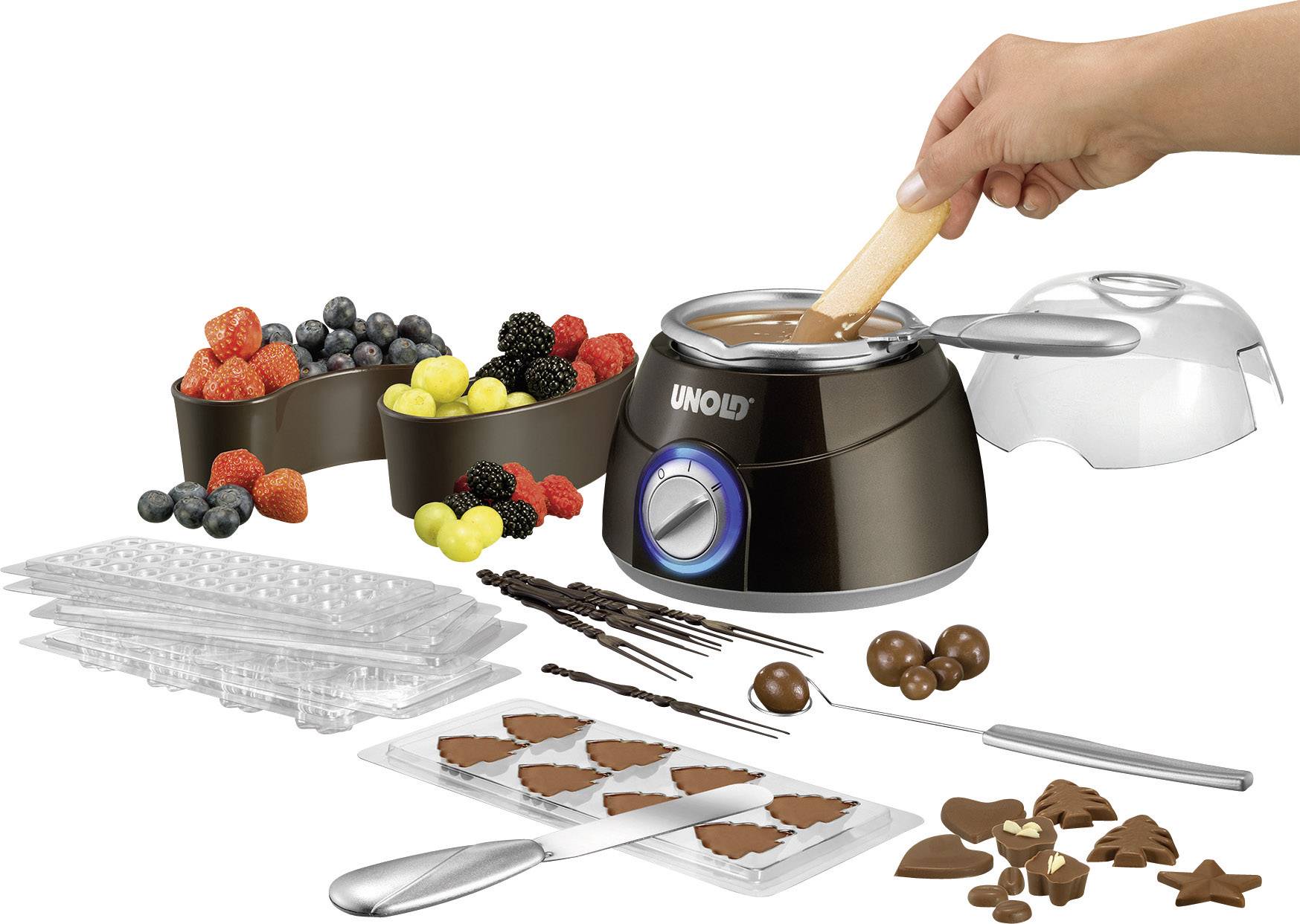 Une machine à fondre le chocolat avec des fruits, des moules et des ustensiles à chocolat. Une main remue du chocolat fondu.