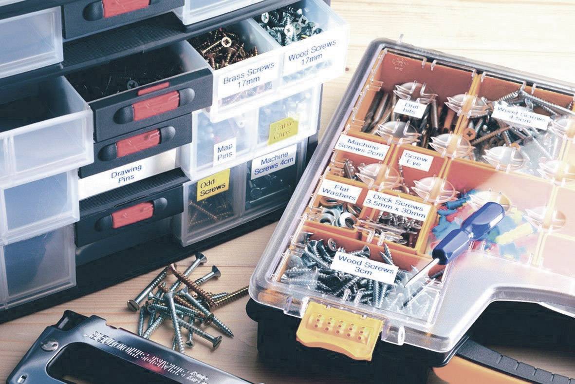 Plusieurs boîtes de rangement pour outils et vis, étiquetées avec différents types. Quelques vis sont éparpillées devant.