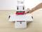 Une main utilise une machine manuelle pour perforer une feuille de papier sur une table.