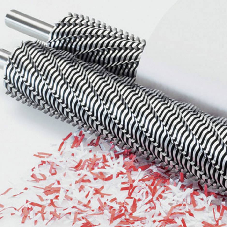 Une machine aux rouleaux tranchants et dentelés déchiquette des bandes de papier rouges et blanches en petits morceaux.