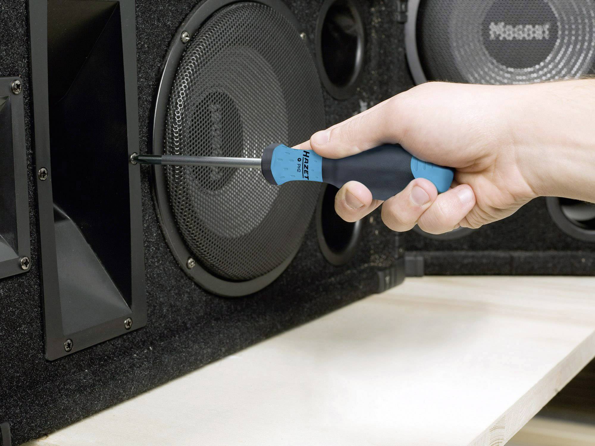 Une main tient un tournevis et serre une vis sur un boîtier d'enceinte noir.